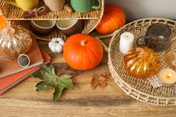 Cups with pumpkins and autumn leaves on table near light wall, closeup