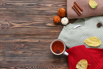 Composition with cup of tea, warm sweaters, candles and autumn leaves on wooden background