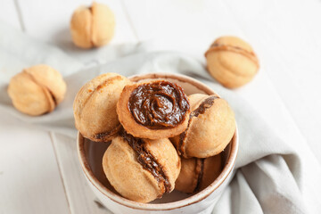 Bowl with sweet walnut shaped cookies with boiled condensed milk on white wooden background