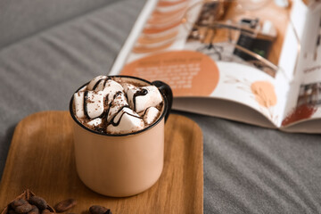 Cup of hot chocolate with marshmallows and magazine on tray in room