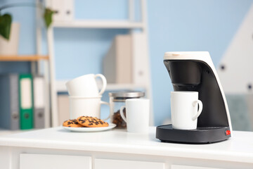 Coffee machine with cups and cookies on table in office, closeup