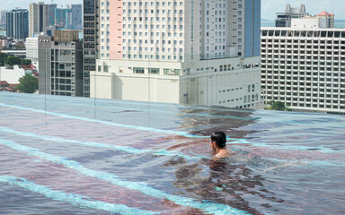 Man swimming in infinity roof top pool. City view at the background.