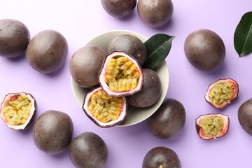 Fresh passion fruits with green leaves on violet background, flat lay