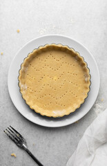 Overhead view of a frozen tart shell in a a tart tin, raw tart pastry crust on white marble countertop, process of making tart