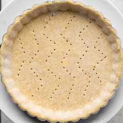  Overhead view of a frozen tart shell in a a tart tin, raw tart pastry crust on white marble countertop, process of making tart