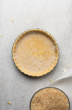  Overhead view of a frozen tart shell in a a tart tin, raw tart pastry crust on white marble countertop, process of making tart