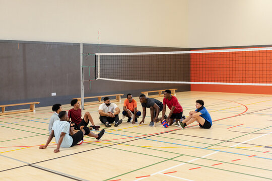 Diverse male volleyball players gathering in semicircle on court talking tactics near net