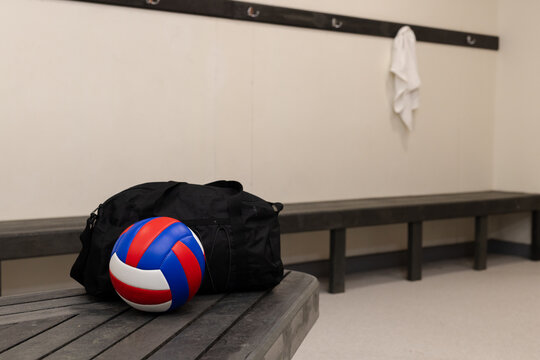 Black duffle bag and red white and blue volleyball resting on bench in locker room