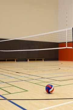Multi-color volleyball resting on court floor under net beside benches, featuring colorful lines