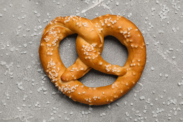 Tasty pretzel with salt on grey grunge background, closeup