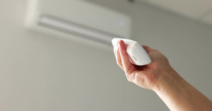 Woman using remote to control air conditioner at home, closeup. Space for text