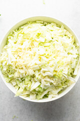 Overhead view of sliced cabbage on a marble countertop, top view of cabbage leaves being shredded, green cabbage being sliced