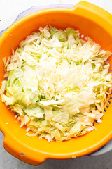 Overhead view of sliced cabbage on a marble countertop, top view of cabbage leaves being shredded, green cabbage being sliced