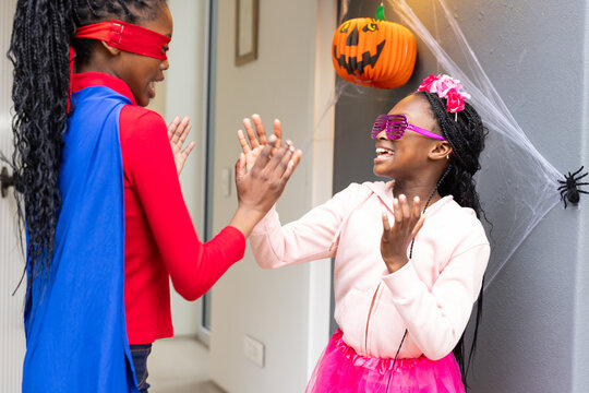 African American girls clapping in Halloween costumes by door with jack-o-lantern and spiderweb