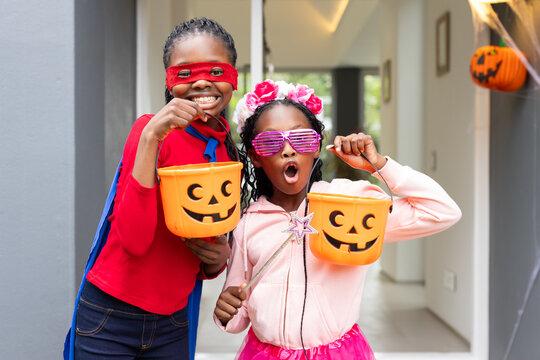 African American girls standing at doorway wearing masks and capes while holding pumpkin buckets