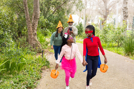 Two African American girls walking on park trail carrying pumpkin buckets in Halloween costumes
