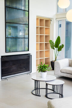nested round coffee tables are sitting on floor in living area, with potted plant and fireplace