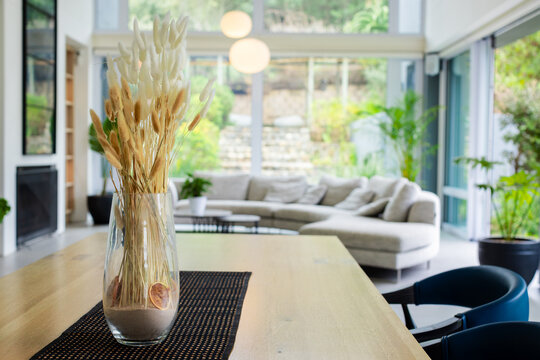 Glass vase holding dried grasses and bunny tails is sitting on dining table by sliding doors