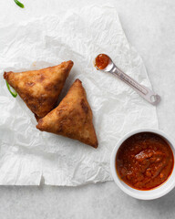 Overhead view of samosa with dip on parchment paper, top view of beef samosa on a white background