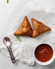 Overhead view of samosa with dip on parchment paper, top view of beef samosa on a white background