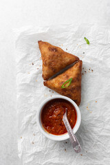 Overhead view of samosa with dip on parchment paper, top view of beef samosa on a white background
