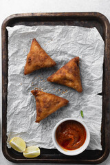 Overhead view of samosa with dip on parchment paper, top view of beef samosa on a white background