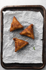 Overhead view of samosa with dip on parchment paper, top view of beef samosa on a white background