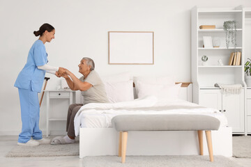 Fototapeta premium Female caregiver helping happy senior woman to stand up in bedroom
