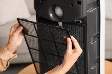 Young woman changing filter in modern air purifier at home, closeup