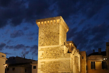 Torre histórica de piedra que se alza en el centro de una plaza al anochecer.  El cielo es de un...