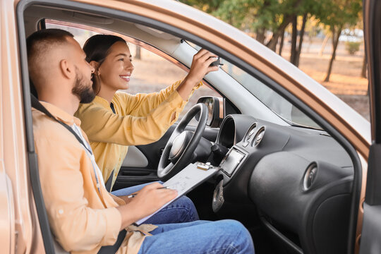 Young woman adjusting mirror before passing driving license test with instructor in car