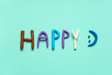 Word HAPPY made of play dough on light blue background