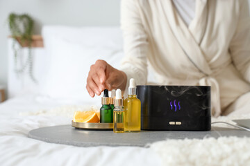 Young woman with air humidifier and essential oils in bedroom, closeup