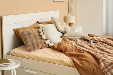 Comfortable bed with pillows and blanket near beige wall in bedroom, closeup