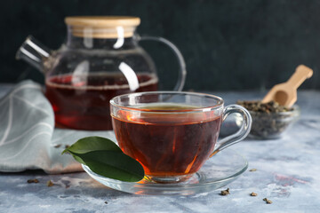 Cup of tasty black tea and green leaves on blue grunge background, closeup