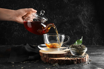 Young woman pouring black tea from teapot into cup on black grunge background