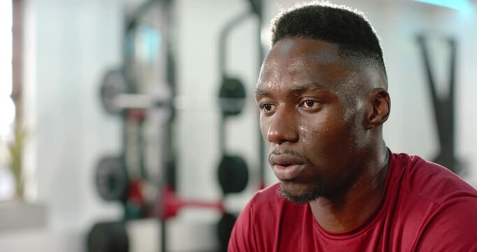 Workout interview prompt causing African American man blinking then speaking near squat rack in gym