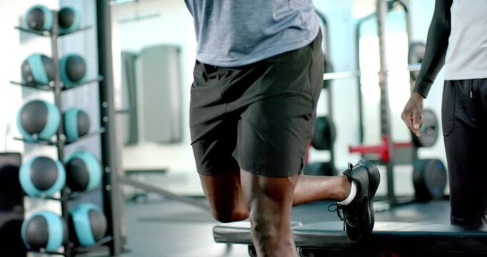 Coach guiding African American man stepping on bench at gym doing split squat for strength