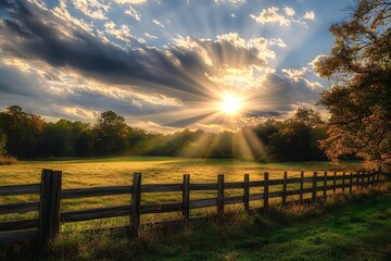 Obraz premium Sun Rays Shining Through Clouds Over Field with Wooden Fence and Trees Landscape