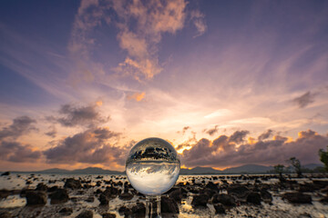  A mesmerizing sunset over a rocky shoreline captured through a glass crystal ball, creating a...