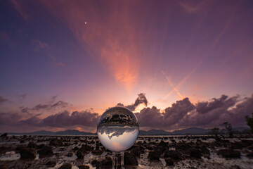  A mesmerizing sunset over a rocky shoreline captured through a glass crystal ball, creating a...