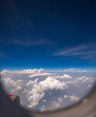 View from airplane window scattered white clouds floating above a vast landscape, with winding...