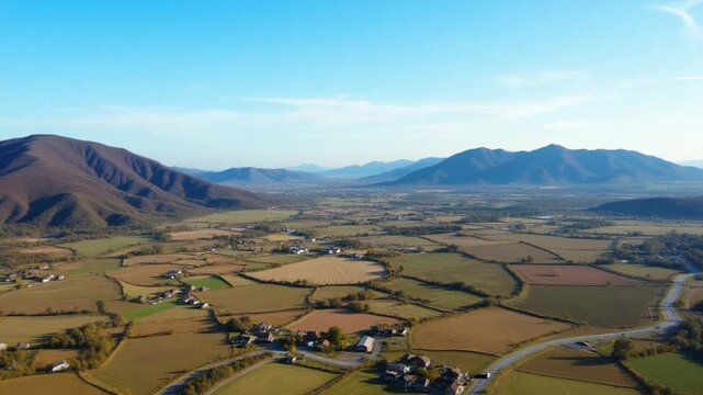 Aerial view of a rural landscape with winding road, houses, and mountains under a blue sky