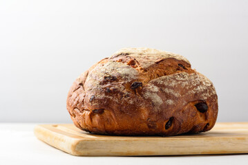 Freshly baked sourdough bread placed on a brown wooden cutting board on a white background