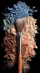 Cosmetic brush atop a heap of colorful powder eyeshadows, ranging from blue to tan, against a solid black background
