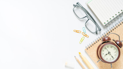 Stylish workspace flatlay featuring a vintage alarm clock, notebook, and glasses on a clean white surface, perfect for back to school, study, or office themes