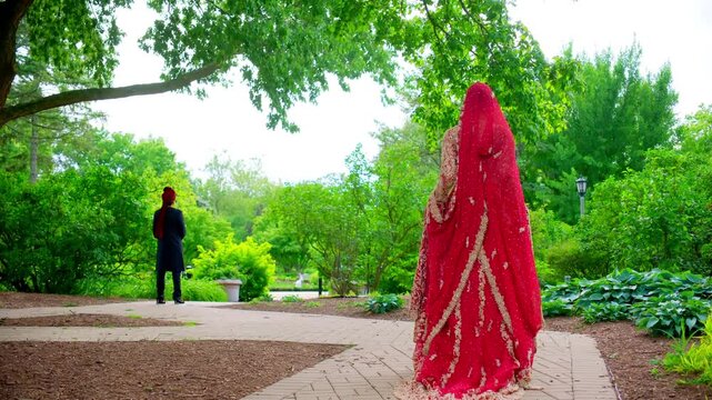 Bride and groom first look at the beautiful park . Red and black colors in the Indian embroidered clothes, Elements of Asian wedding. 