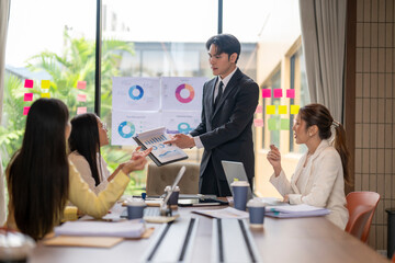 Asian businessman showing charts on clipboard during office meeting