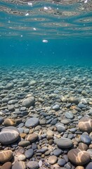 Clear, tranquil underwater view of a shallow riverbed, revealing smooth, colorful stones bathed in sunlight filtering through the water.