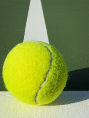 Close up tennis ball beside a crisp white line on a green court, sunlit texture and clean horizontal sports background for banners and headers